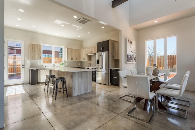 kitchen with appliances with stainless steel finishes, a kitchen bar, a center island, and a healthy amount of sunlight