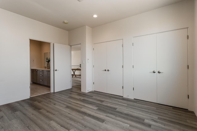 unfurnished bedroom featuring connected bathroom, hardwood / wood-style floors, and two closets