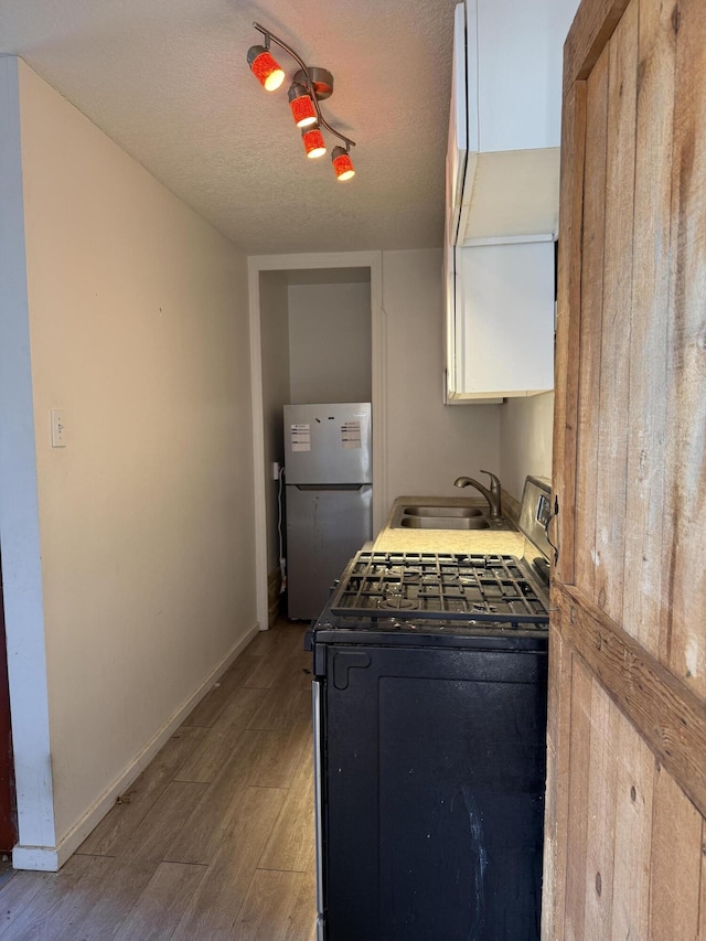 kitchen with a sink, baseboards, range with gas stovetop, light wood-type flooring, and freestanding refrigerator