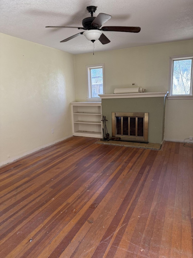 unfurnished living room with a textured ceiling, a ceiling fan, hardwood / wood-style floors, and a glass covered fireplace