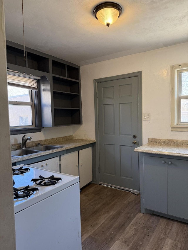 kitchen featuring white gas range oven, white cabinets, dark wood finished floors, light countertops, and a sink