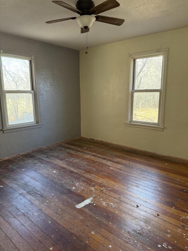spare room with a wealth of natural light, a textured wall, a textured ceiling, and hardwood / wood-style floors