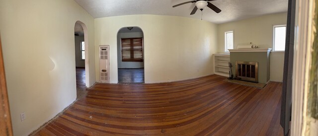 unfurnished room with arched walkways, a ceiling fan, hardwood / wood-style floors, vaulted ceiling, and a textured ceiling