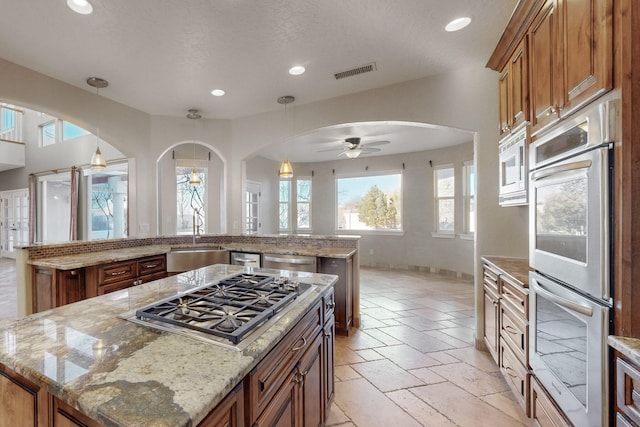 kitchen with sink, stainless steel appliances, light stone countertops, and a kitchen island