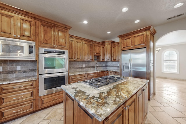 kitchen featuring light stone counters, stainless steel appliances, a center island, and decorative backsplash