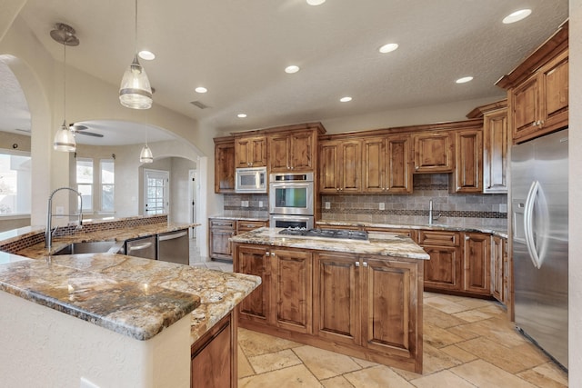 kitchen with sink, hanging light fixtures, stainless steel appliances, light stone countertops, and a kitchen island