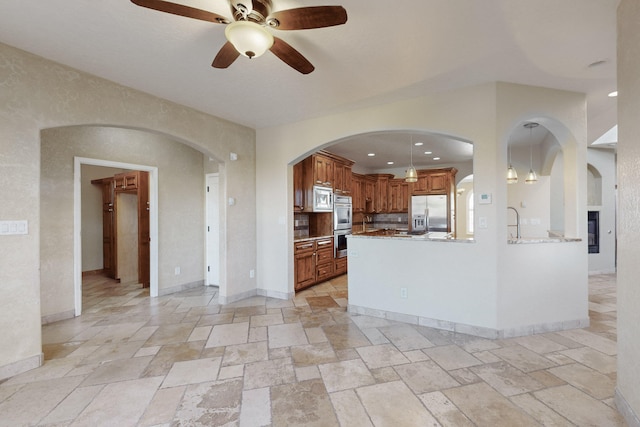 kitchen featuring kitchen peninsula, hanging light fixtures, light stone counters, ceiling fan, and stainless steel appliances