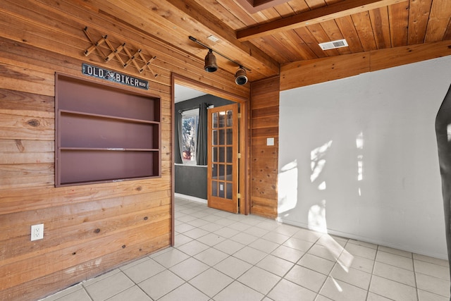 empty room with beam ceiling, tile patterned floors, wood ceiling, and wooden walls