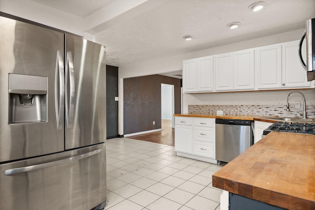 kitchen with stainless steel appliances, butcher block counters, sink, and white cabinets