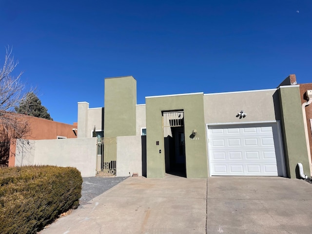 pueblo revival-style home with stucco siding, concrete driveway, an attached garage, a gate, and fence