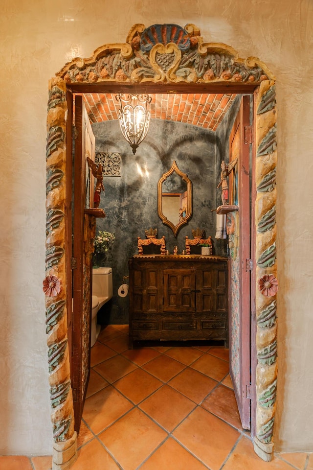 corridor with tile patterned flooring, brick ceiling, and a notable chandelier