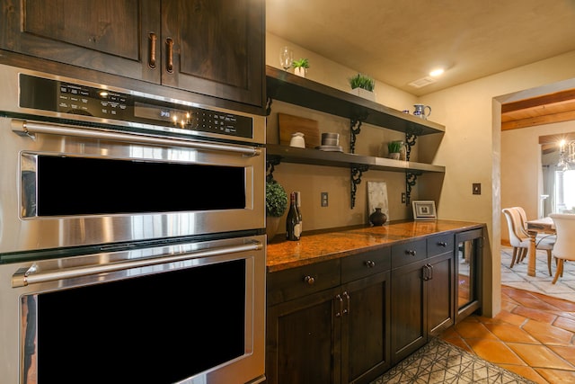 kitchen with dark stone countertops, stainless steel double oven, wine cooler, and dark brown cabinetry