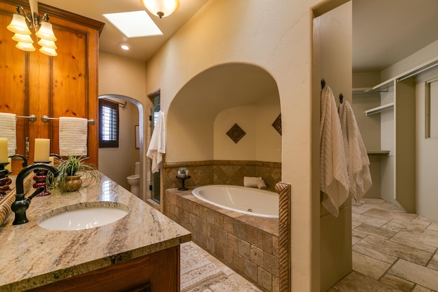 bathroom featuring vanity, toilet, a skylight, and tiled tub