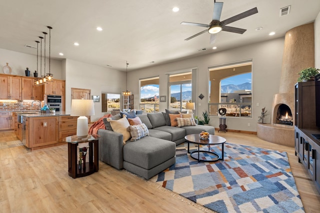 living room featuring sink, light hardwood / wood-style flooring, a towering ceiling, a fireplace, and ceiling fan with notable chandelier