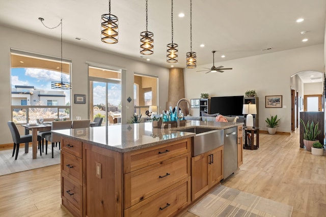 kitchen featuring dishwasher, sink, hanging light fixtures, a kitchen island with sink, and light stone countertops