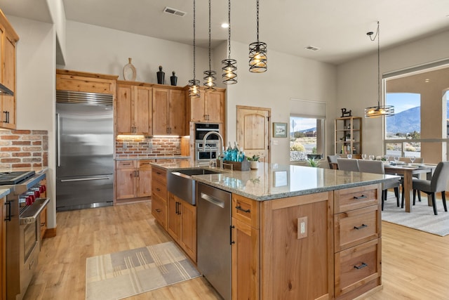 kitchen with high end appliances, sink, a center island with sink, and pendant lighting