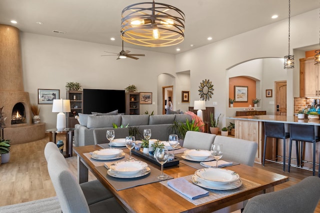 dining area with ceiling fan with notable chandelier, a large fireplace, and hardwood / wood-style floors