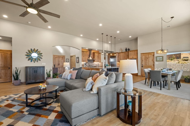 living room with light wood-type flooring, ceiling fan, and a high ceiling