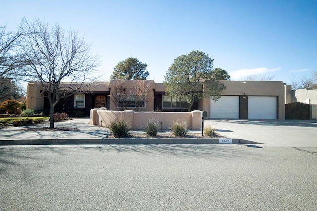 pueblo revival-style home with an attached garage, fence, concrete driveway, and stucco siding