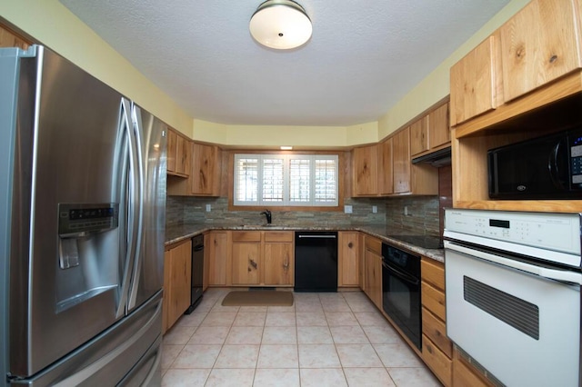 kitchen with light tile patterned floors, a sink, backsplash, dark stone counters, and black appliances