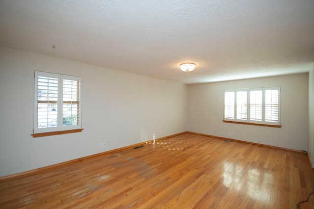 empty room with light wood-style floors, visible vents, plenty of natural light, and baseboards