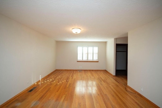 empty room featuring light wood-type flooring, visible vents, and baseboards