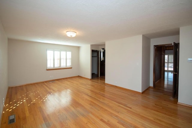 empty room with a healthy amount of sunlight, visible vents, light wood-style flooring, and baseboards