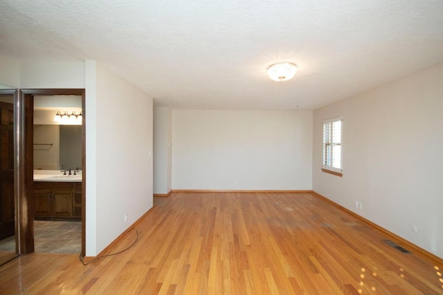 unfurnished room featuring light wood-type flooring, visible vents, a sink, and baseboards