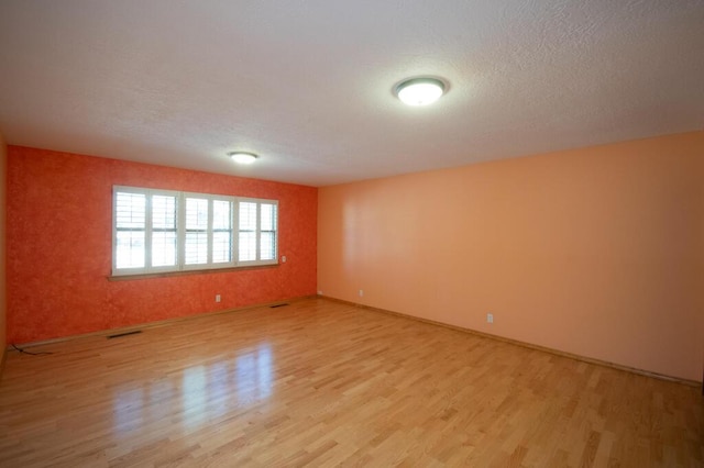 empty room featuring light wood finished floors, baseboards, and a textured ceiling