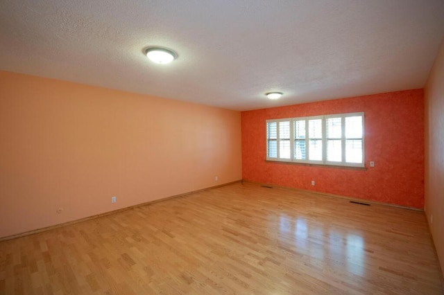 unfurnished room featuring a textured ceiling, visible vents, light wood-style flooring, and baseboards