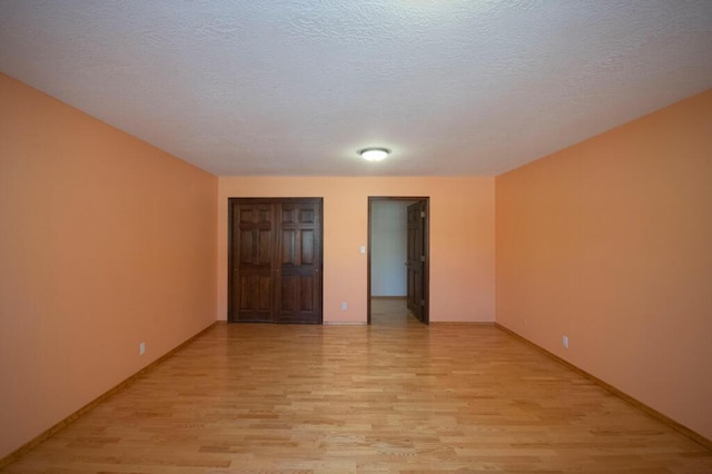 interior space featuring light wood-type flooring, a textured ceiling, and baseboards