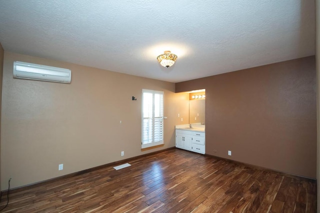 unfurnished bedroom with a textured ceiling, a wall unit AC, dark wood finished floors, and baseboards