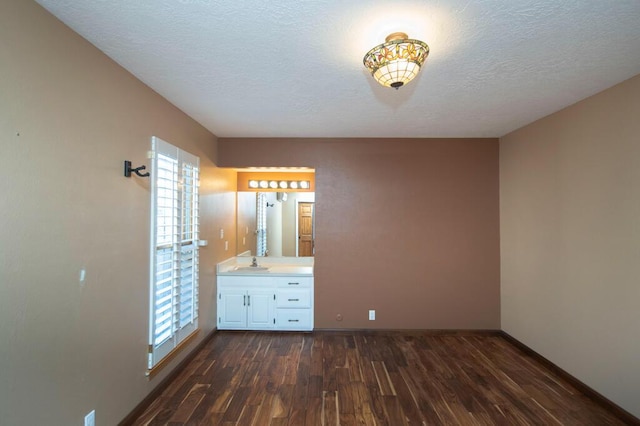 unfurnished bedroom featuring multiple windows, dark wood finished floors, a textured ceiling, and a sink