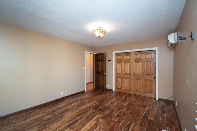 unfurnished bedroom with a textured ceiling, a wall unit AC, baseboards, a closet, and dark wood finished floors