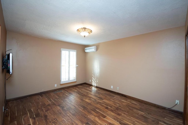 empty room featuring a textured ceiling, dark wood-type flooring, a wall mounted air conditioner, and baseboards