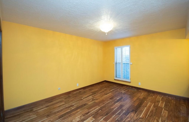 spare room with a textured ceiling, dark wood-type flooring, and baseboards