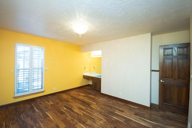 spare room featuring a textured ceiling, dark wood finished floors, built in study area, and baseboards