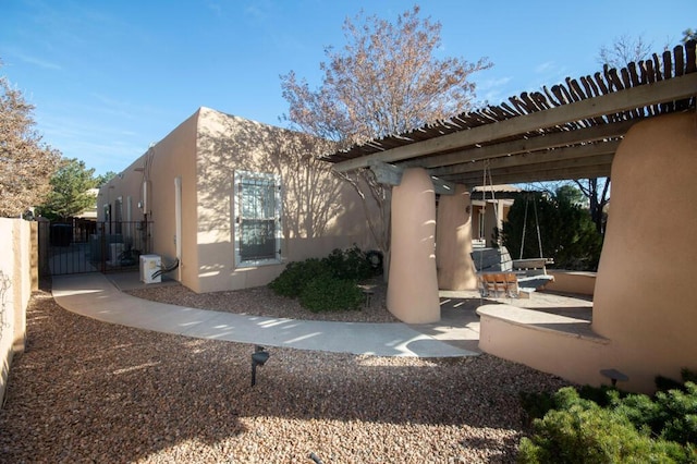 view of home's exterior with a gate, fence, a patio area, a pergola, and stucco siding