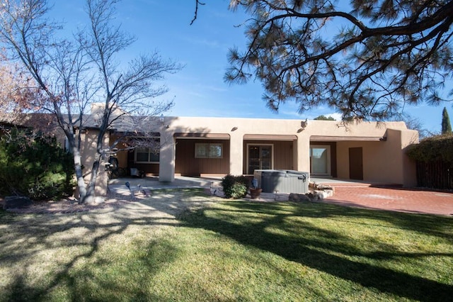 back of house with a yard, a hot tub, and stucco siding