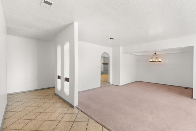 carpeted spare room with a notable chandelier and a textured ceiling