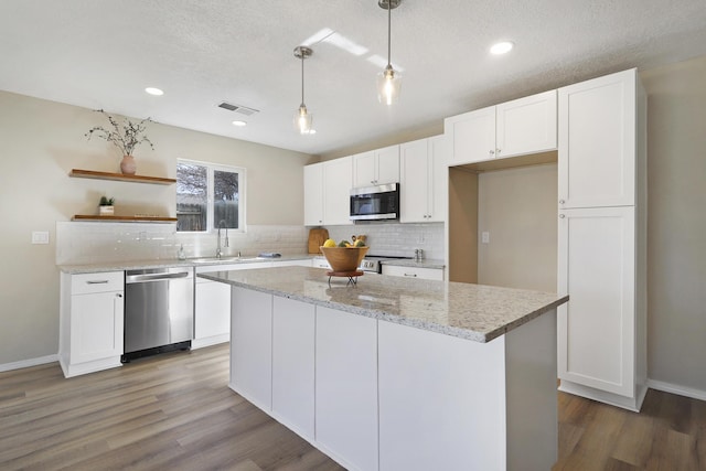 kitchen with light stone counters, decorative light fixtures, a kitchen island, stainless steel appliances, and white cabinets