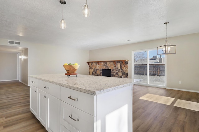 kitchen with white cabinetry, a textured ceiling, hanging light fixtures, a kitchen island, and hardwood / wood-style flooring