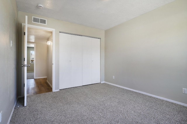 unfurnished bedroom featuring a closet, a textured ceiling, and dark colored carpet