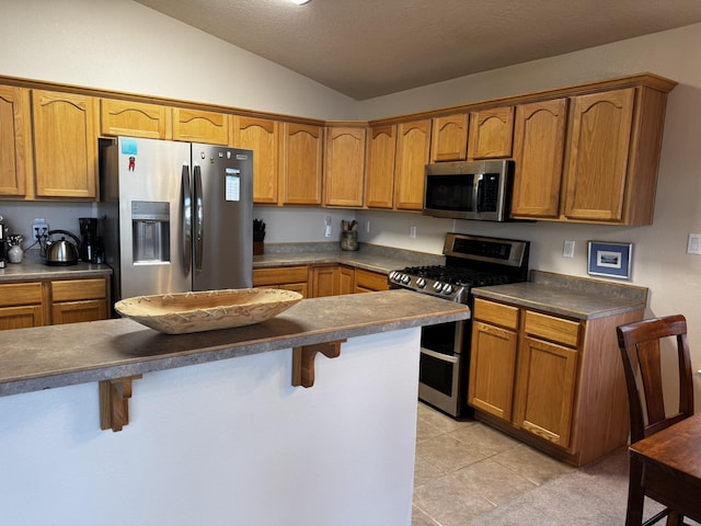 kitchen with vaulted ceiling, appliances with stainless steel finishes, a kitchen breakfast bar, light tile patterned floors, and a textured ceiling