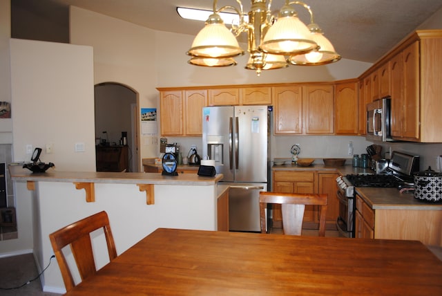 kitchen with appliances with stainless steel finishes, lofted ceiling, a kitchen breakfast bar, a notable chandelier, and kitchen peninsula