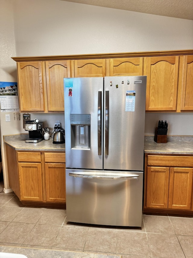 kitchen featuring stainless steel refrigerator with ice dispenser, light tile patterned flooring, and a textured ceiling