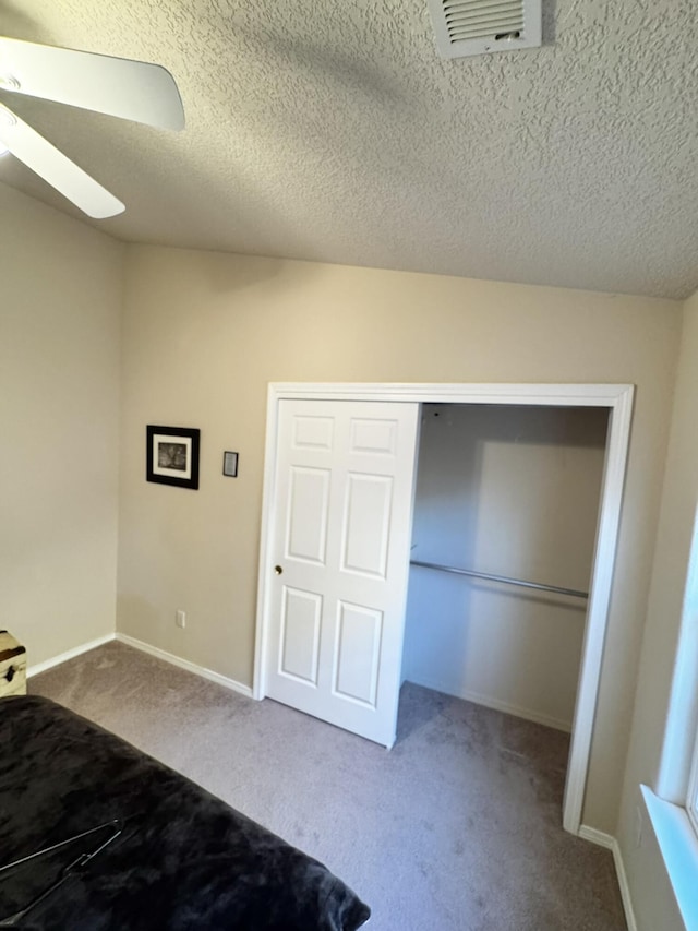 unfurnished bedroom with a textured ceiling, a closet, ceiling fan, and carpet