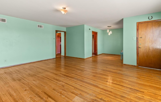 spare room with an inviting chandelier and light hardwood / wood-style floors