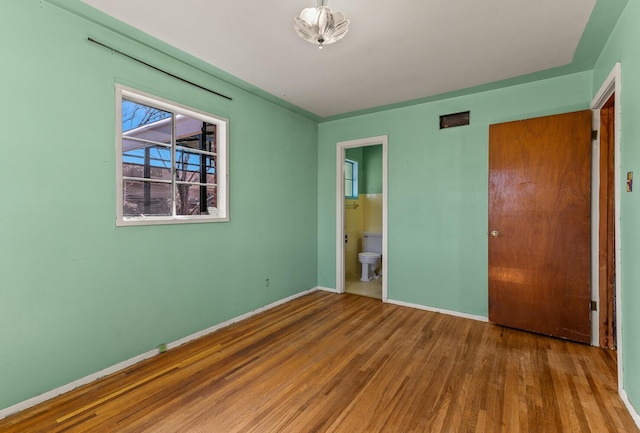 unfurnished bedroom featuring ensuite bathroom and hardwood / wood-style floors