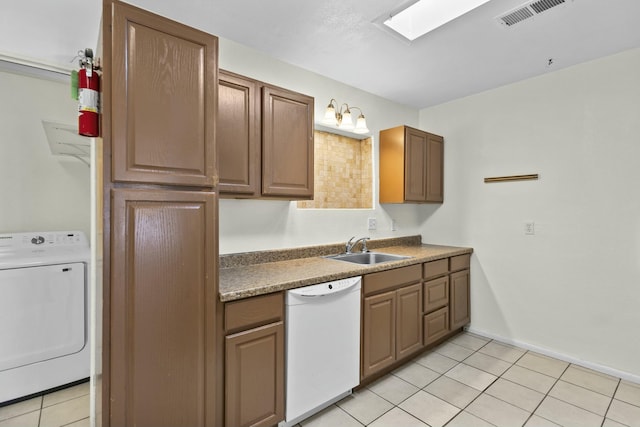 kitchen with light tile patterned floors, sink, a skylight, white dishwasher, and washer / clothes dryer